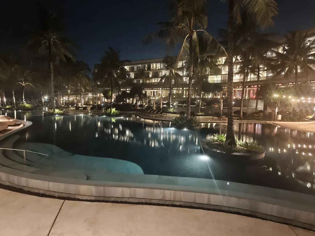 Curved swimming pool lit up at night surrounded by palms