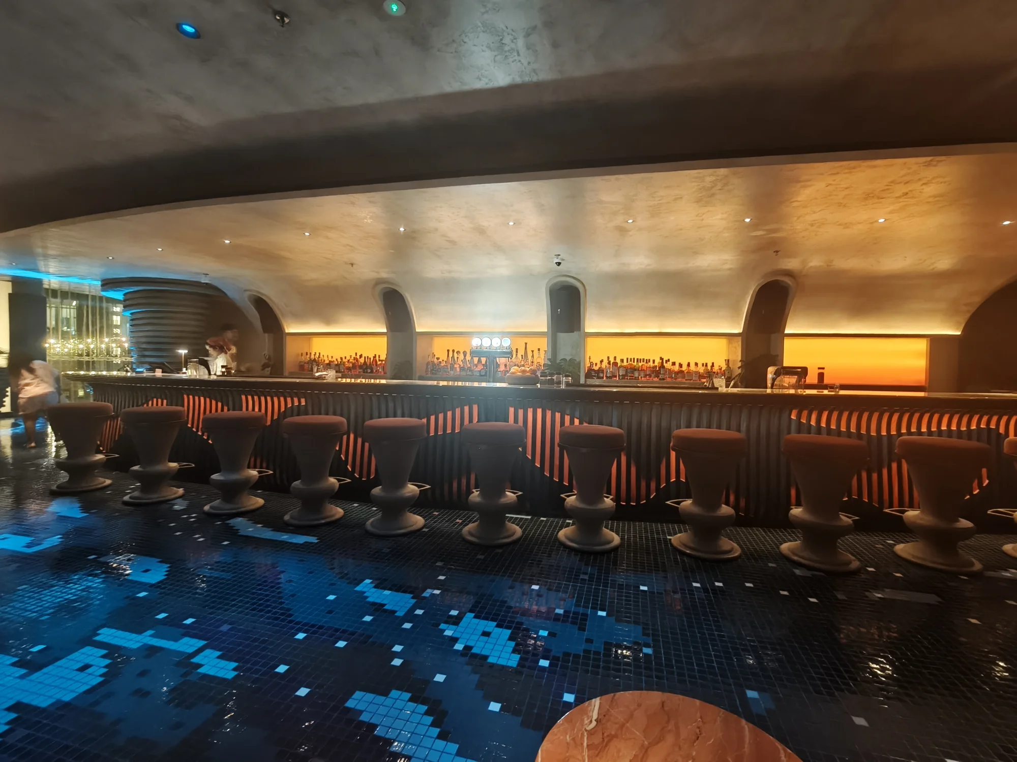 Long bar with blue mosaic floor and warm lighting at Alune Beach Club