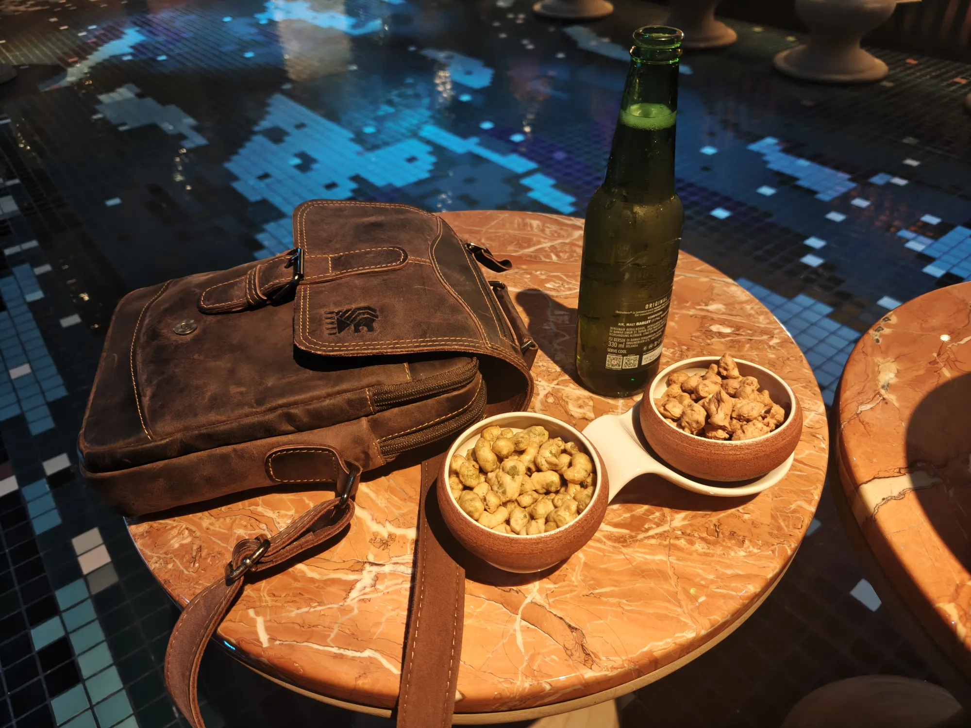 Beer bottle and bowls of nuts on a marble table at Alune Beach Club