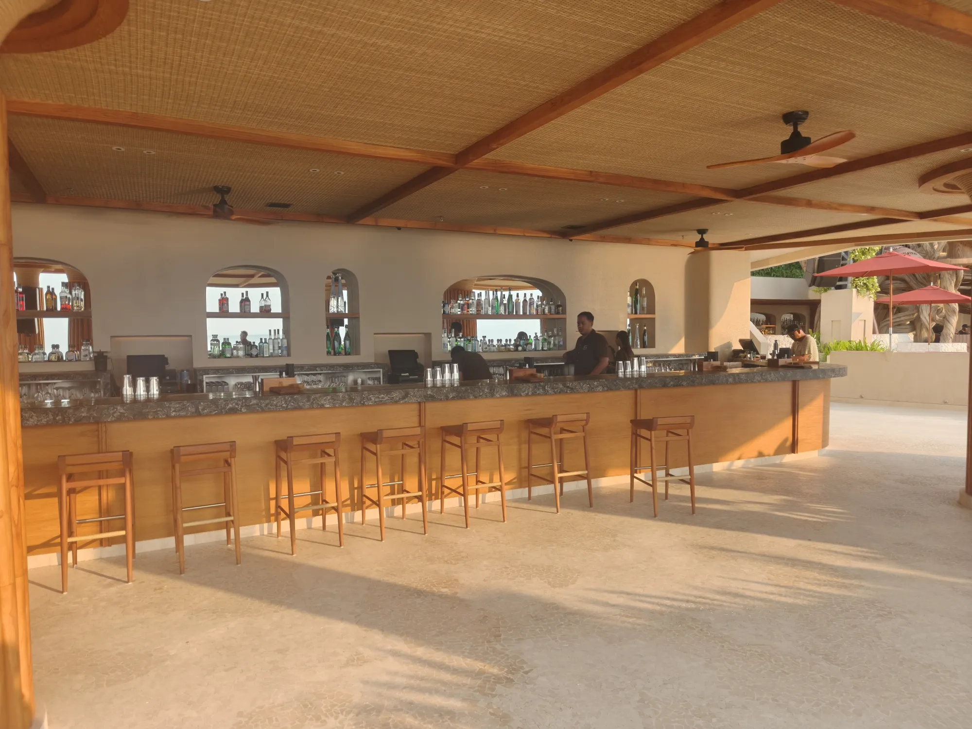 Long indoor bar with wooden stools and ceiling fans